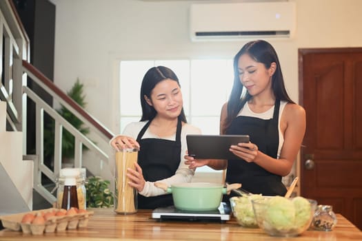 Mother and her daughter review recipe on a tablet while preparing meal in a kitchen.