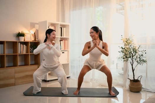 Asian mom and her teen daughter doing yoga workout at home.