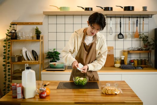 Young man pours dressing onto a bowl of fresh vegetable salad.