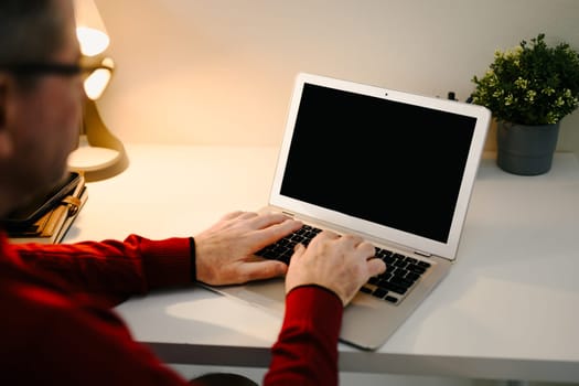 Close p of an older man hands typing on a laptop with a black screen.