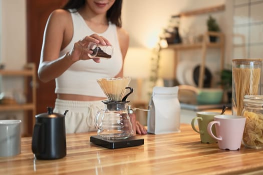 Young woman preparing pour over coffee using a glass dripper in a warmly home kitchen.