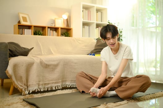 Smiling man in casual clothes doing warm up exercise on yoga mat.