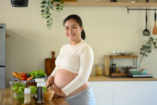 Happy pregnant woman stands at kitchen counter, preparing a wholesome meal.