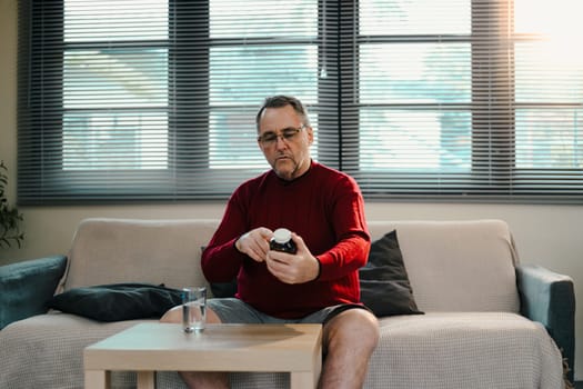 Mature man reviews the instructions on a bottle of pills with a glass of water on the table.