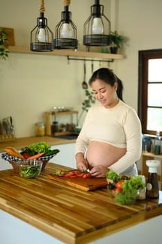 Happy pregnant woman stands at kitchen counter, preparing a wholesome meal.