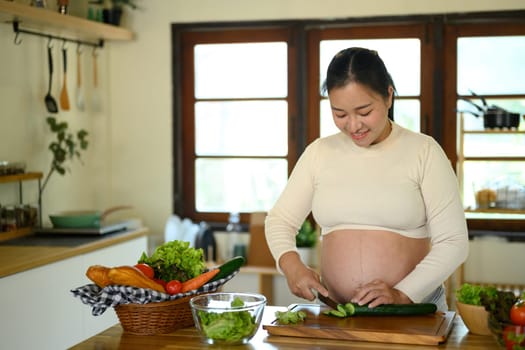 Happy pregnant woman stands at kitchen counter, preparing a wholesome meal.
