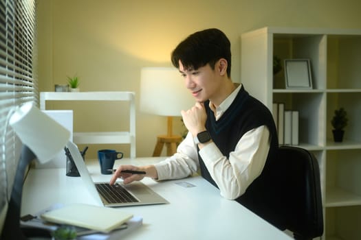 Young entrepreneur in a sweater vest uses a laptop at a minimalist desk.