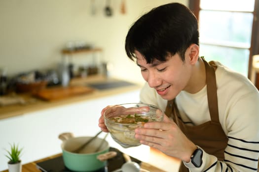 Hands seen seasoning a clear broth soup with meatballs and herbs.