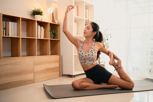 Beautiful asian woman practicing elegant yoga stretches in a peaceful living room.