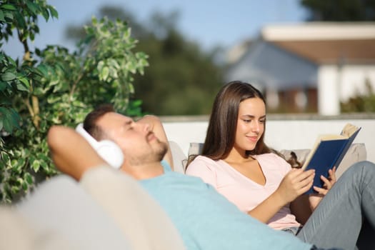 Couple enjoying of different hobbies sitting in couch in a terrace at home