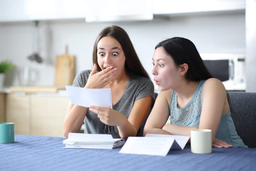 Amazed interracial women checking bank statement in the kitchen at home