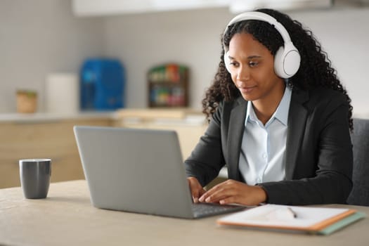 Black executive tele working with laptop and headphone in the kitchen at home