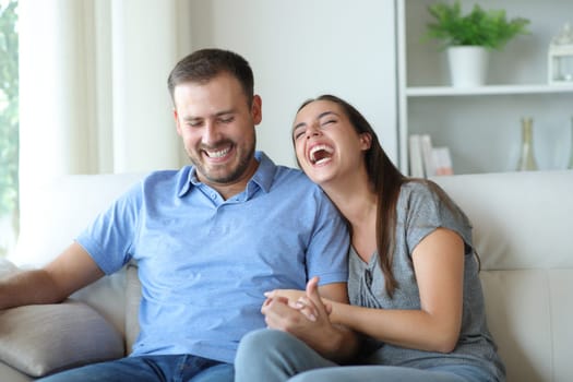 Couple at home laughing hilariously sitting on a couch