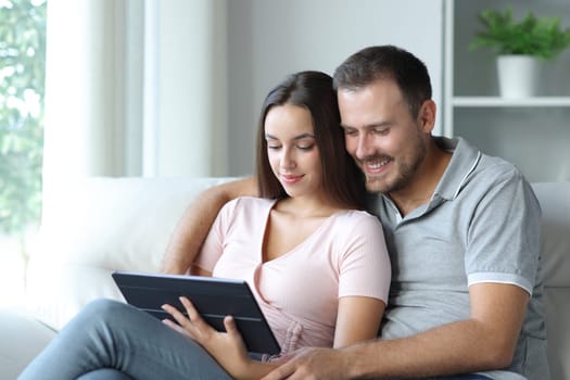Couple watching media on tablet sitting in a sofa at home