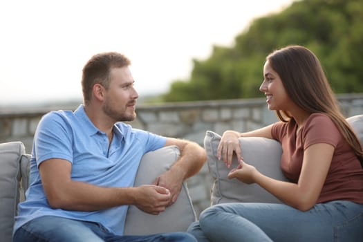 Couple or freinds talking sitting in a couch in a terrace at home