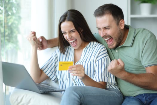 Excited couple buying amazing products online with laptop and credit card at home