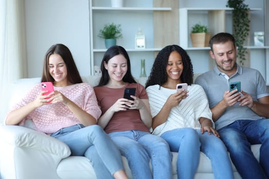 Front view portrait of four happy friends using everyone their phones at home