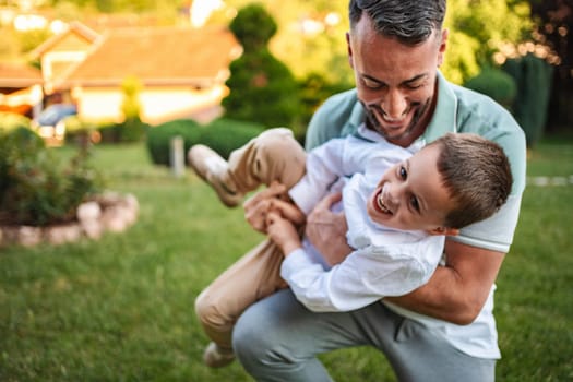 A father lifts his giggling son in a lively garden.