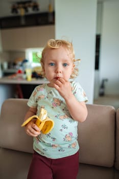 Little one relishes fresh banana while exploring indoors.