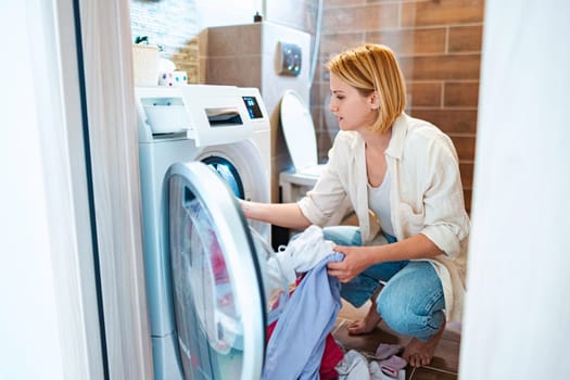 Woman carefully arranging clothes in a washing machine.