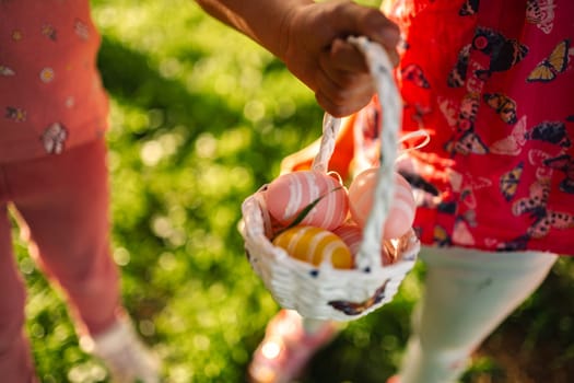 Two children explore a vibrant green field, holding a basket filled with beautifully decorated eggs. The sun shines brightly, creating a cheerful atmosphere perfect for Easter celebrations.