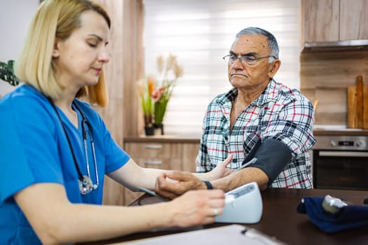 A nurse measures the blood pressure of an older patient indoors.