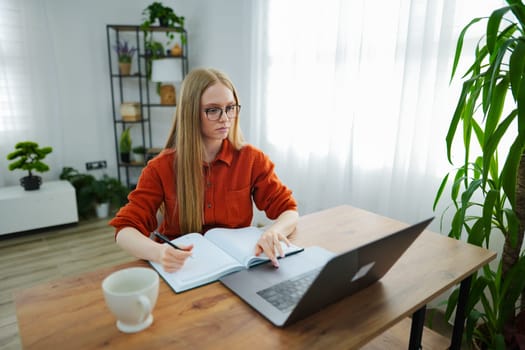 A young woman intently studies at her desk, surrounded by plants and light.
