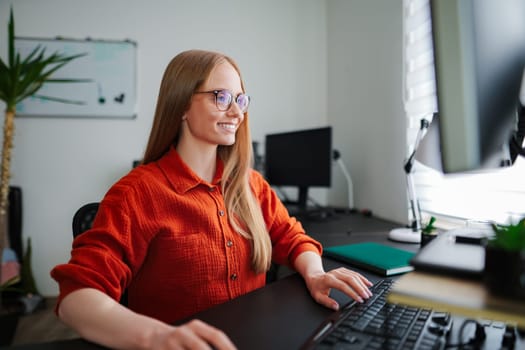 Brightly lit workspace features a smiling woman working intently on a computer.