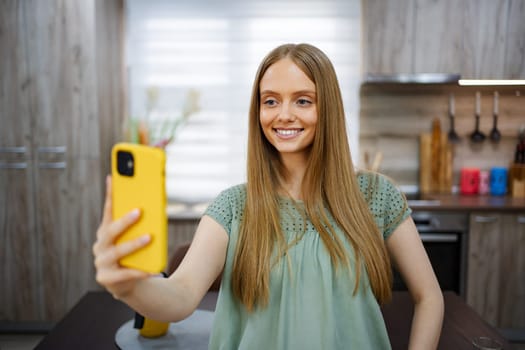 Young woman happily taking a selfie in a stylish kitchen setting.