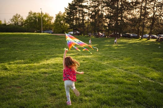 In a vibrant park during golden hour, children race across the lush grass, their laughter filling the air as they fly bright kites that dance in the wind, creating a picturesque moment of joy.
