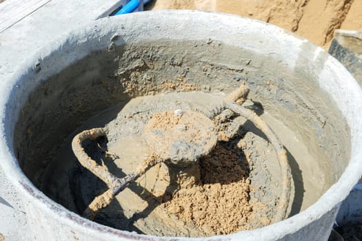 Cement mixer filled with gray mortar and tan sand, blades churning to create a construction-ready concrete mix.
