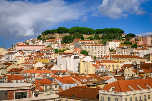 Scenic view of Lisbon, Portugal, historic St George castle on top of hill, traditional Portuguese architecture with red-tiled roofs and colorful houses on sunny day with bright blue sky and some clouds. Famous travel destination, summer vacation