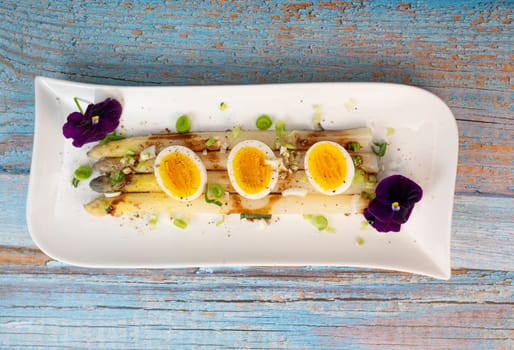 Baked asparagus with boiled egg in big white plate on blue background. High quality photo