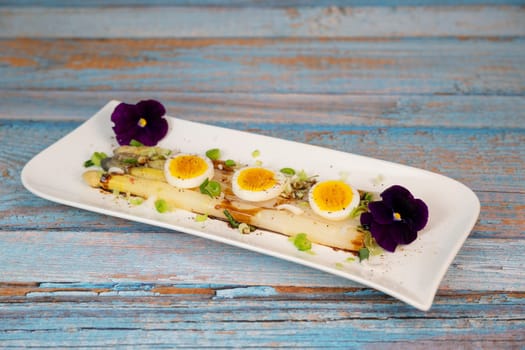 Baked asparagus with boiled egg in big white plate on blue background. High quality photo