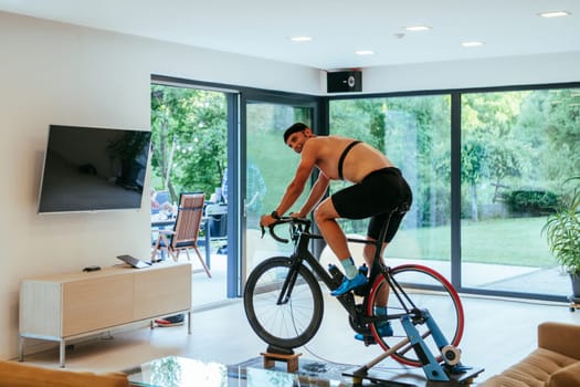 A triathlete riding a triathlon bike on a machine simulation in a modern living room.