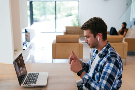 A freelancer sitting at a table in a modern living room, with headphones using a laptop for business video chat, conversation with friends and entertainment.