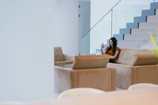 A woman using a smartphone for a video call while sitting in a modern house