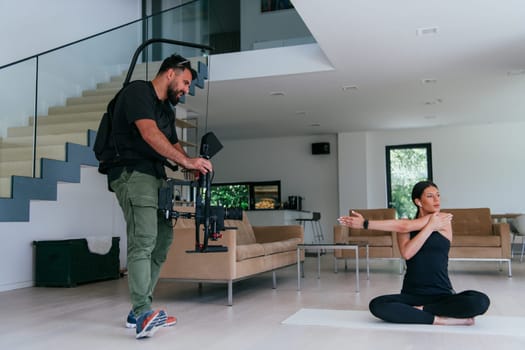 Behind the scene. Photo of a cameraman recording a woman doing yoga exercises at an online training while using and watching a laptop
