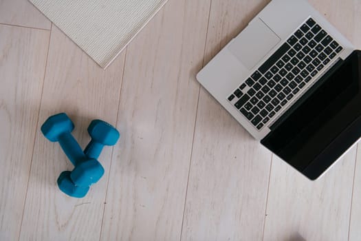 Photo of a laptop, dumbbells and headphones on the floor of the living room. Online training concept