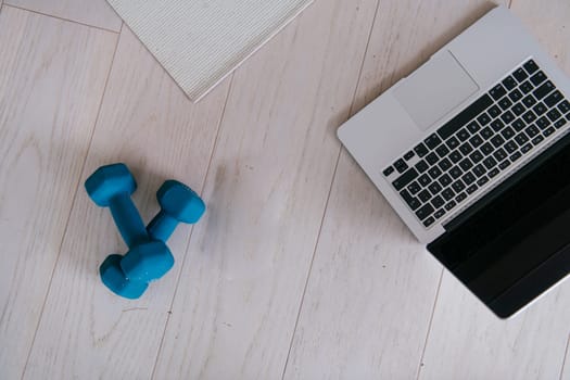Photo of a laptop, dumbbells and headphones on the floor of the living room. Online training concept