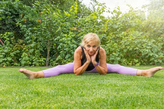 Flexible smiling mature woman  doing a leg split supporting her chin with both hands. Horizontally. 