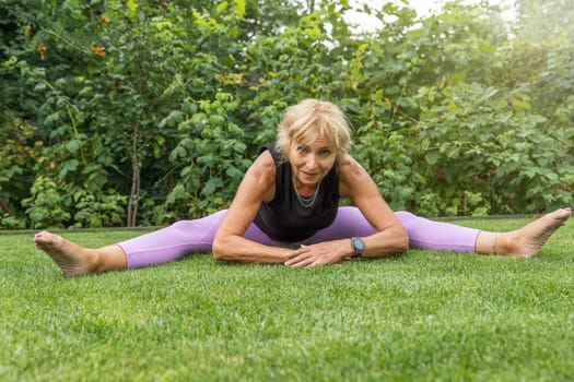 Flexible smiling mature woman  doing a leg split outside. Horizontally. 
