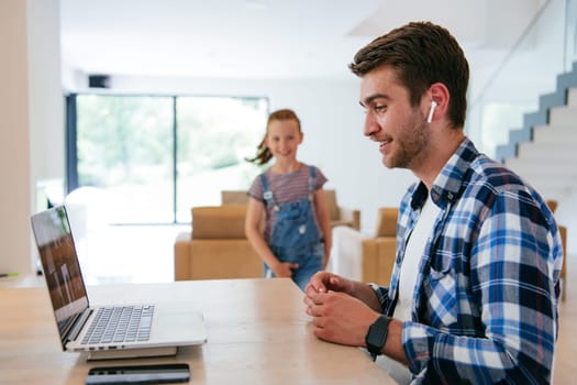 A freelancer sitting at a table in a modern living room, with headphones using a laptop for business video chat, conversation with friends and entertainment.