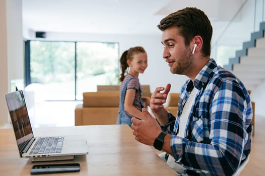 A freelancer sitting at a table in a modern living room, with headphones using a laptop for business video chat, conversation with friends and entertainment.