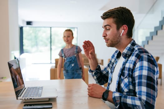 A freelancer sitting at a table in a modern living room, with headphones using a laptop for business video chat, conversation with friends and entertainment.