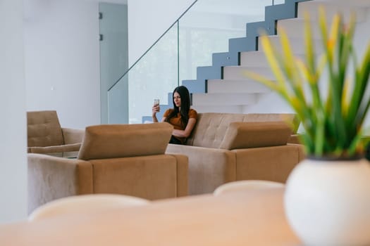 A woman using a smartphone for a video call while sitting in a modern house