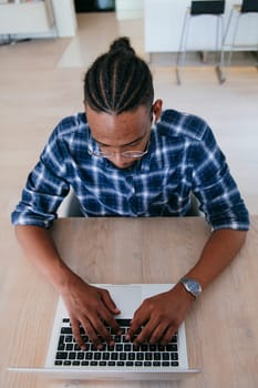Top view of African American businessman in glasses sitting at a table in a modern living room, using a laptop and smartphone for business video chat, conversation with friends and entertainment.