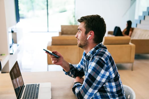 A freelancer sitting at a table in a modern living room, with headphones using a laptop for business video chat, conversation with friends and entertainment.