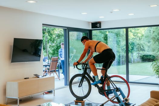 A triathlete riding a triathlon bike on a machine simulation in a modern living room.