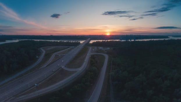 Drone photo of a highway bridge stretching over a river toward a Barnaul city skyline, captured at colorful sunset with clear sky.